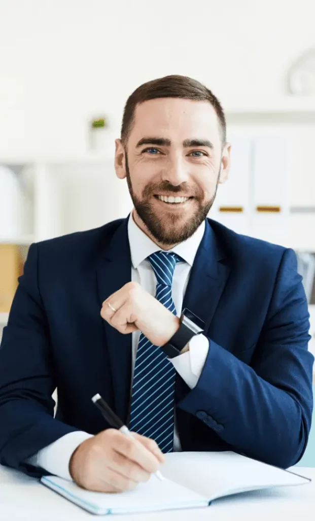 Un directeur général ou PDG assis à son bureau, carnet ouvert et stylo à la main, souriant avec assurance.